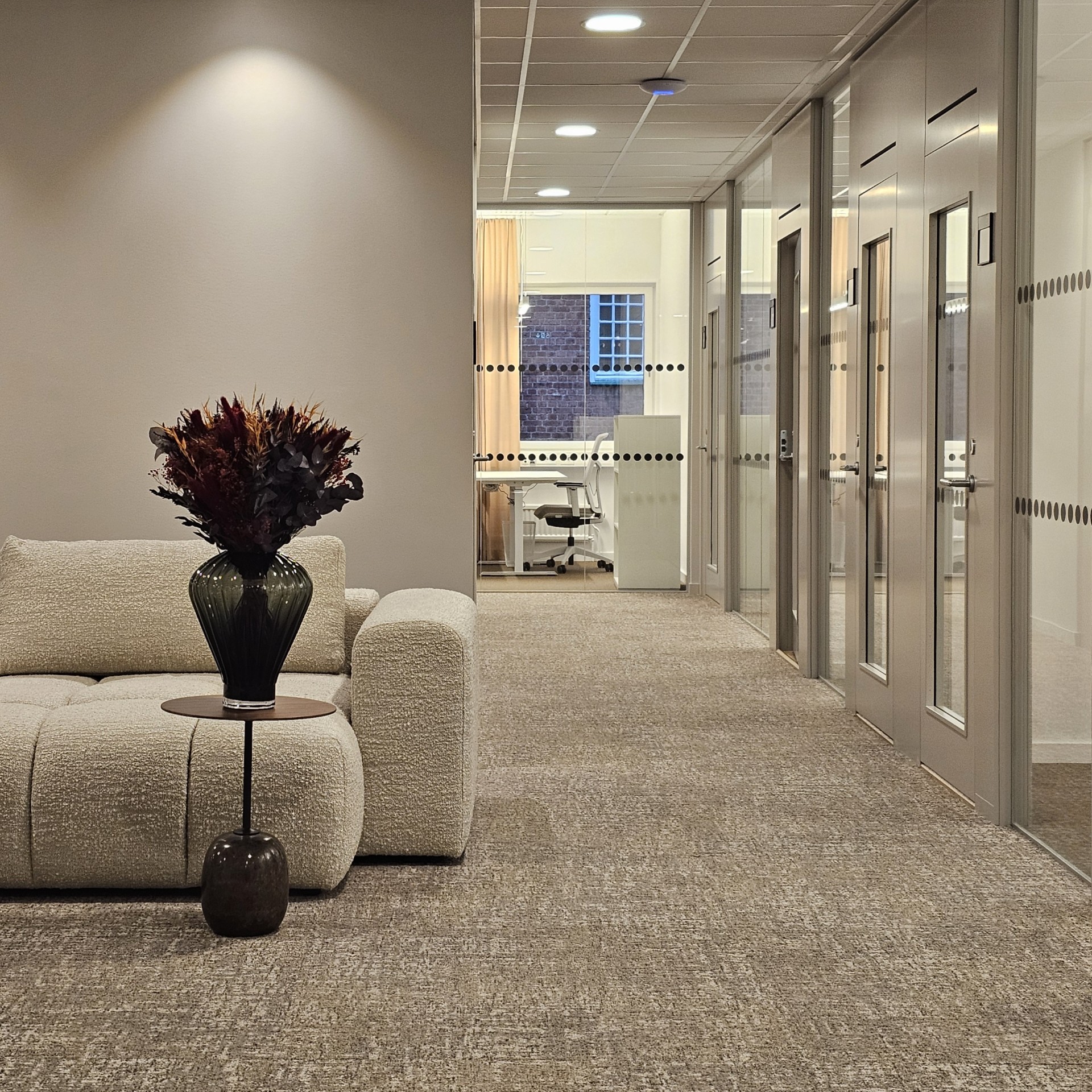 Inbjudande lobby med stor beige soffa, bord, stor vas med bukett och kontorsrum på kontorshotell i Borås.